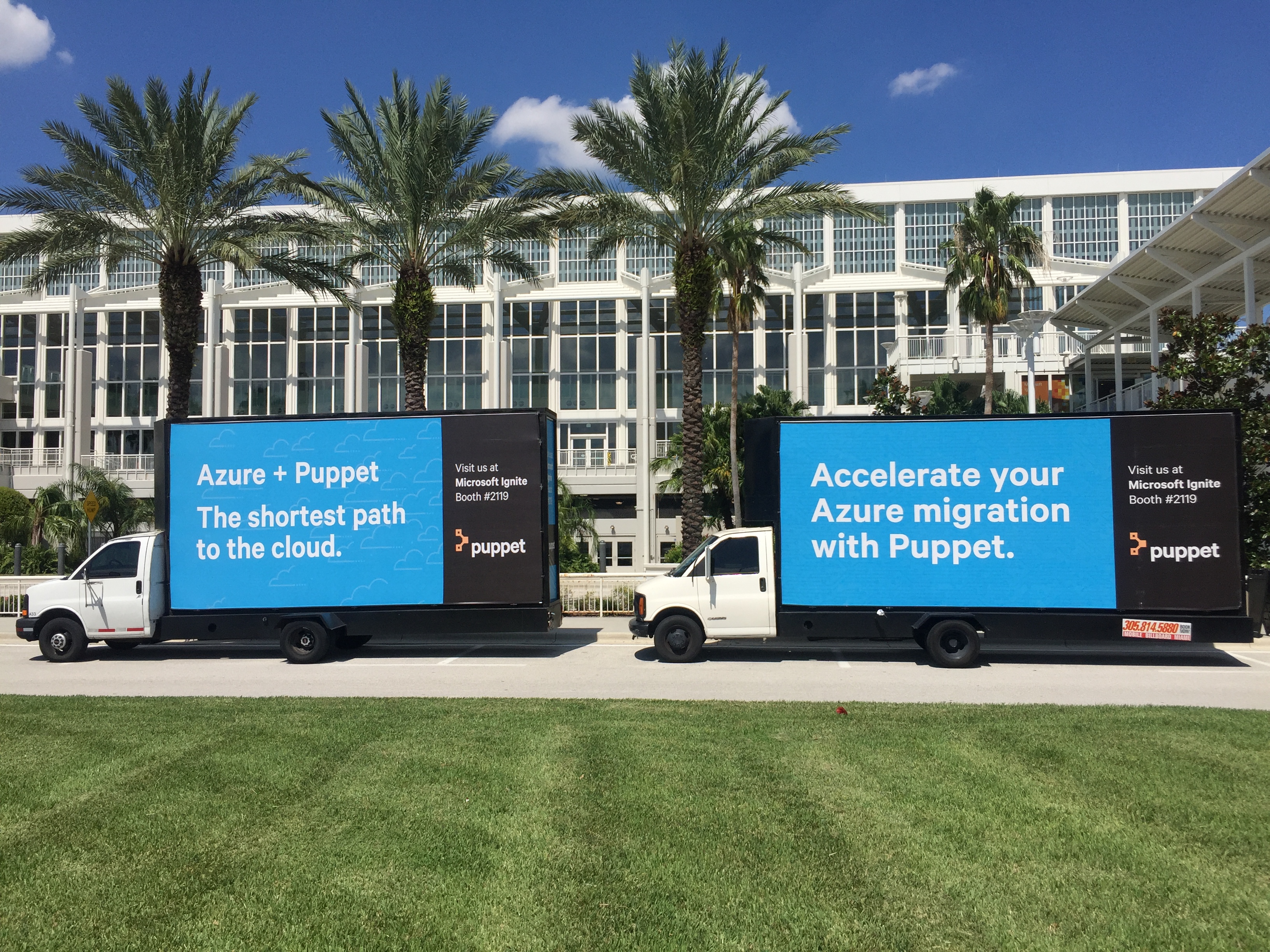 Mobile digital billboard on trucks parked in front of a building with palm trees.